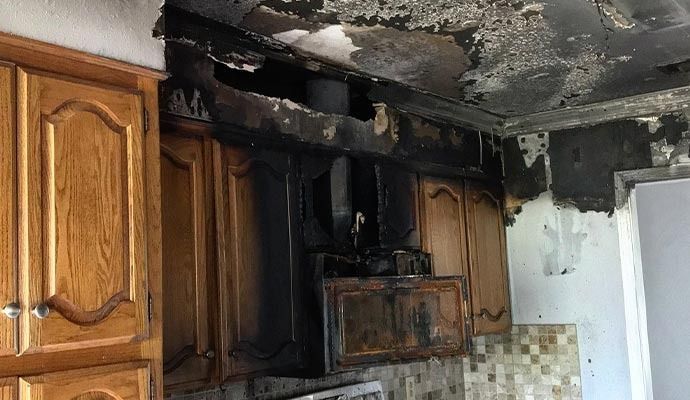 Kitchen cabinets and ceiling damaged by fire; soot and char marks are visible.