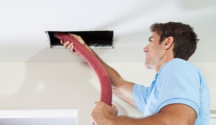 Man cleaning air vent with a vacuum hose.