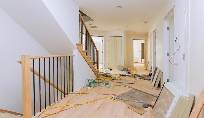 Hallway under renovation with exposed wooden floors, stairs, and construction materials.
