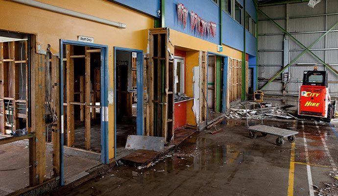 Interior of a building in disrepair, debris on the floor, red forklift to the right.