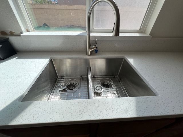 Stainless steel double sink with faucet, white countertop, and window in background.