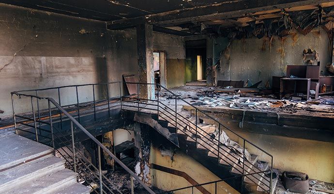 Interior of a burned-out building with stairs, debris, and smoke damage.