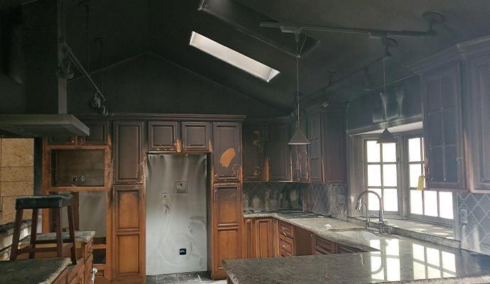 Kitchen interior heavily damaged by fire; soot-covered walls and cabinets, with a skylight and a window.