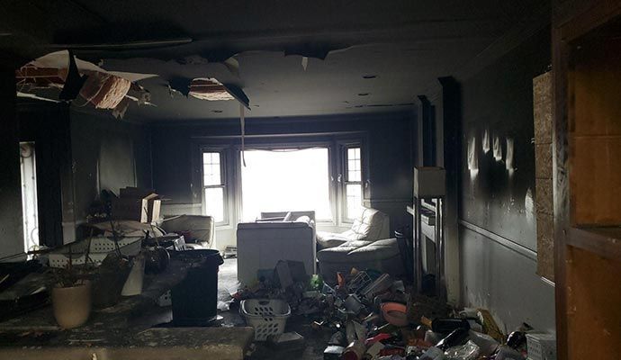 Interior of a room severely damaged by fire; visible debris, charring, and light streaming in from windows.