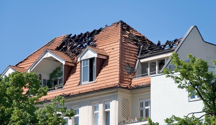 Roof of a building with visible fire damage, charred wood, and missing sections. Blue sky.