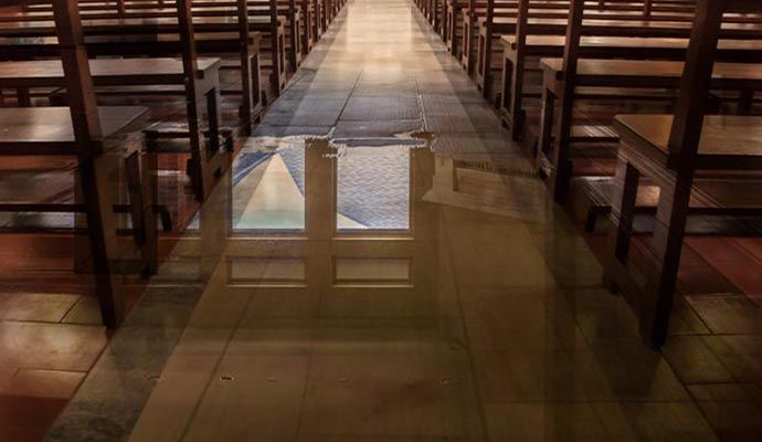 Rows of wooden chairs line a church aisle with the reflection of windows on the floor.