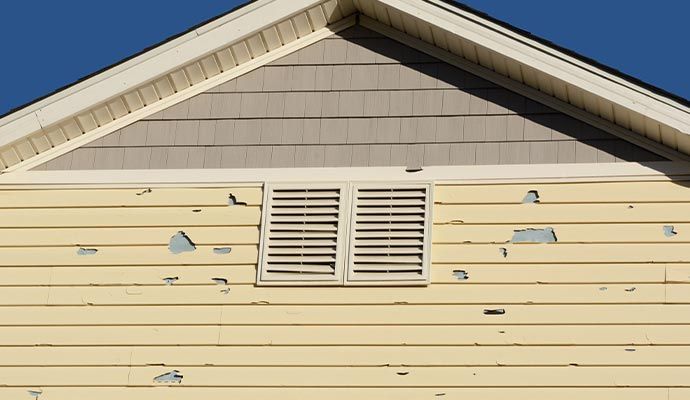 Yellow house siding with peeling paint and a vent.
