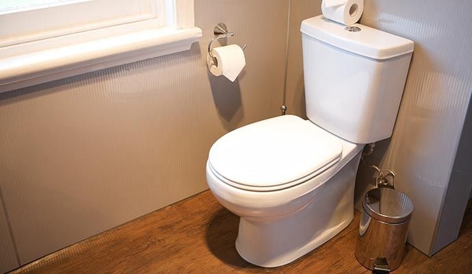 White toilet in a bathroom with a window, toilet paper holder, and trash can.