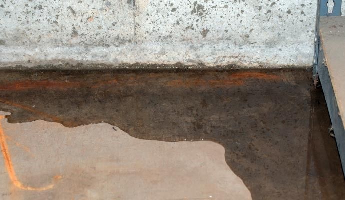 Wet, dark surface along a concrete wall. Rust-colored line and dark pooling water visible.