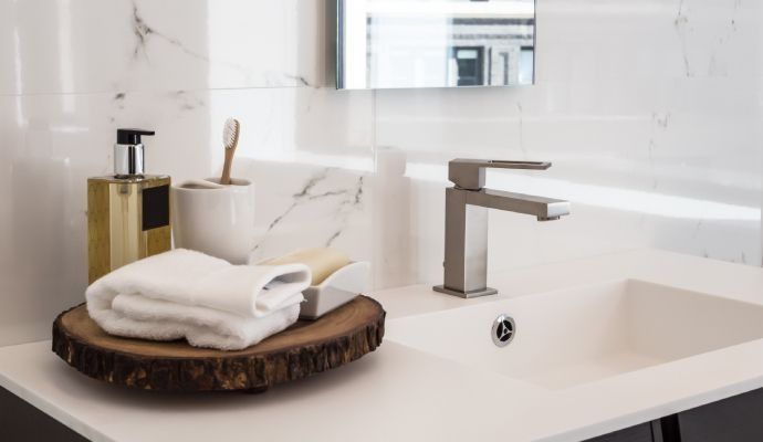 Bathroom sink with white countertop, faucet, and toiletries displayed on a wood slab.