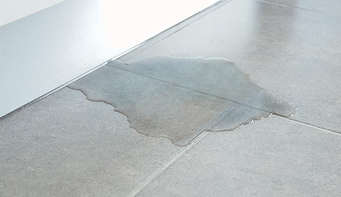 Water puddle on gray tiled floor, near the edge of a white object, likely a door.