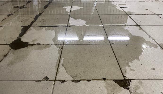 Water pooled on dirty, light-colored tiled floor with a bright light reflecting above.