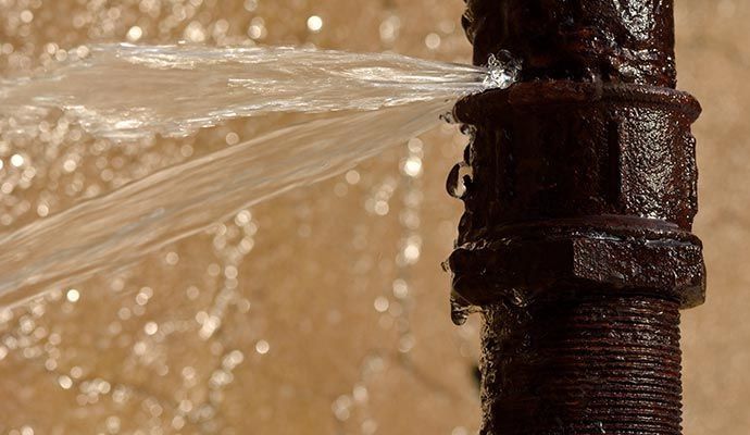 Rusty pipe with a water leak, spraying outwards.