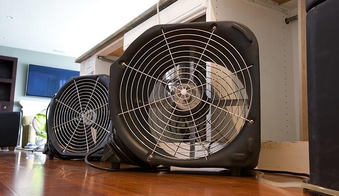 Two black box fans on a hardwood floor, one closer and larger than the other.