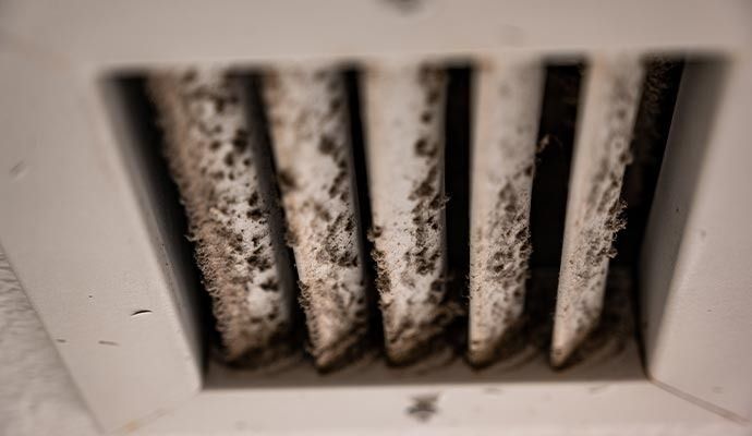 Close-up of a white air vent with visible accumulation of dirt and debris between the slats.