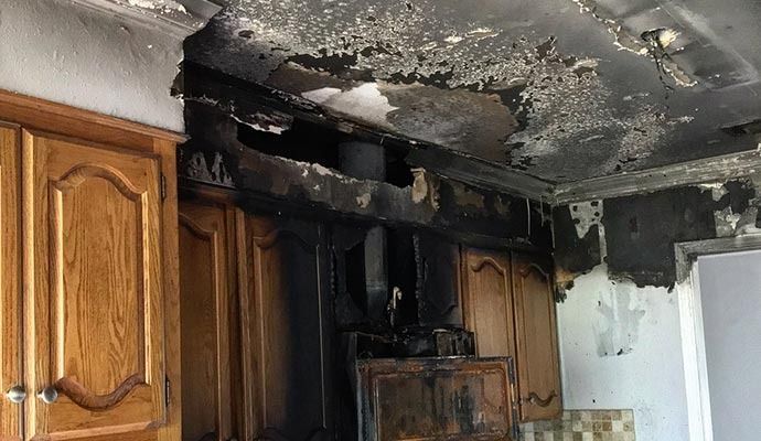 Charred kitchen interior: damaged cabinets, burnt ceiling, and appliance after a fire.
