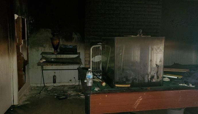 Interior view of a smoke-damaged room with a table, appliances, and charred walls.