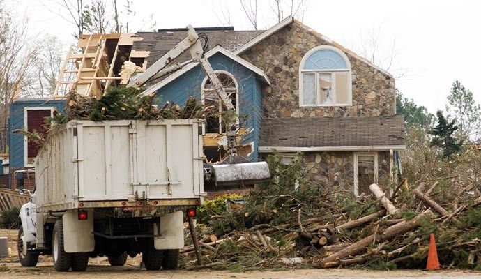 Debris from tree and roof damage being loaded into a truck in front of a house.