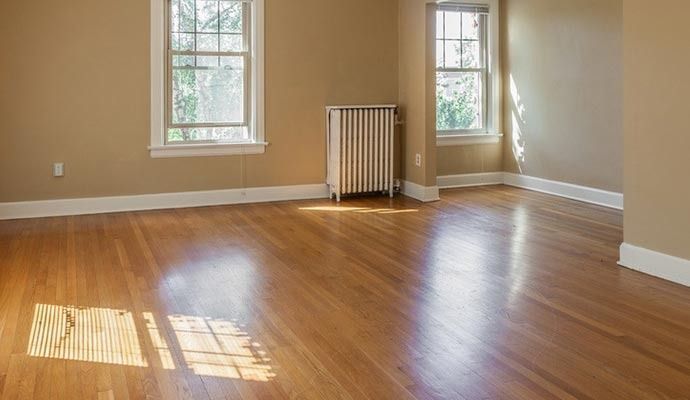 Empty room with hardwood floors, beige walls, two windows, and radiator.