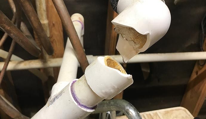Broken white PVC pipes in a cluttered attic, with exposed interior and brown discoloration.
