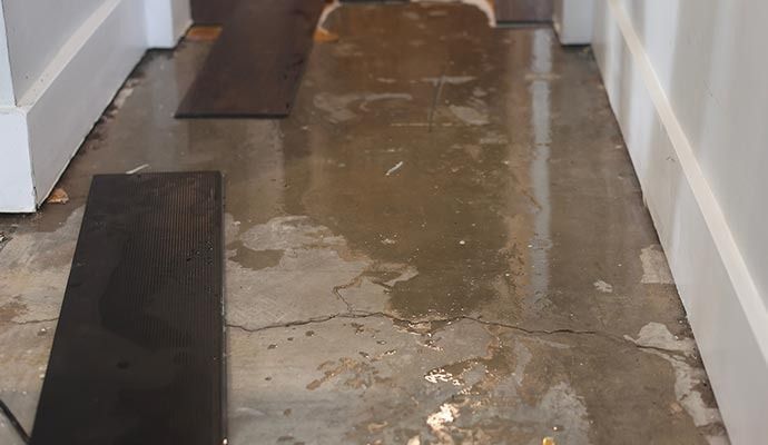 Wet concrete floor with visible cracks, some dark wood planks, and white trim.