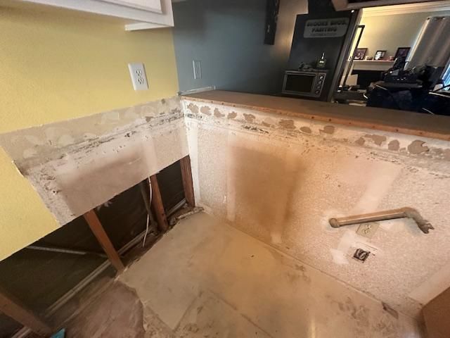 Kitchen renovation in progress: bare walls, exposed framing, countertop removed, and electrical outlets visible.