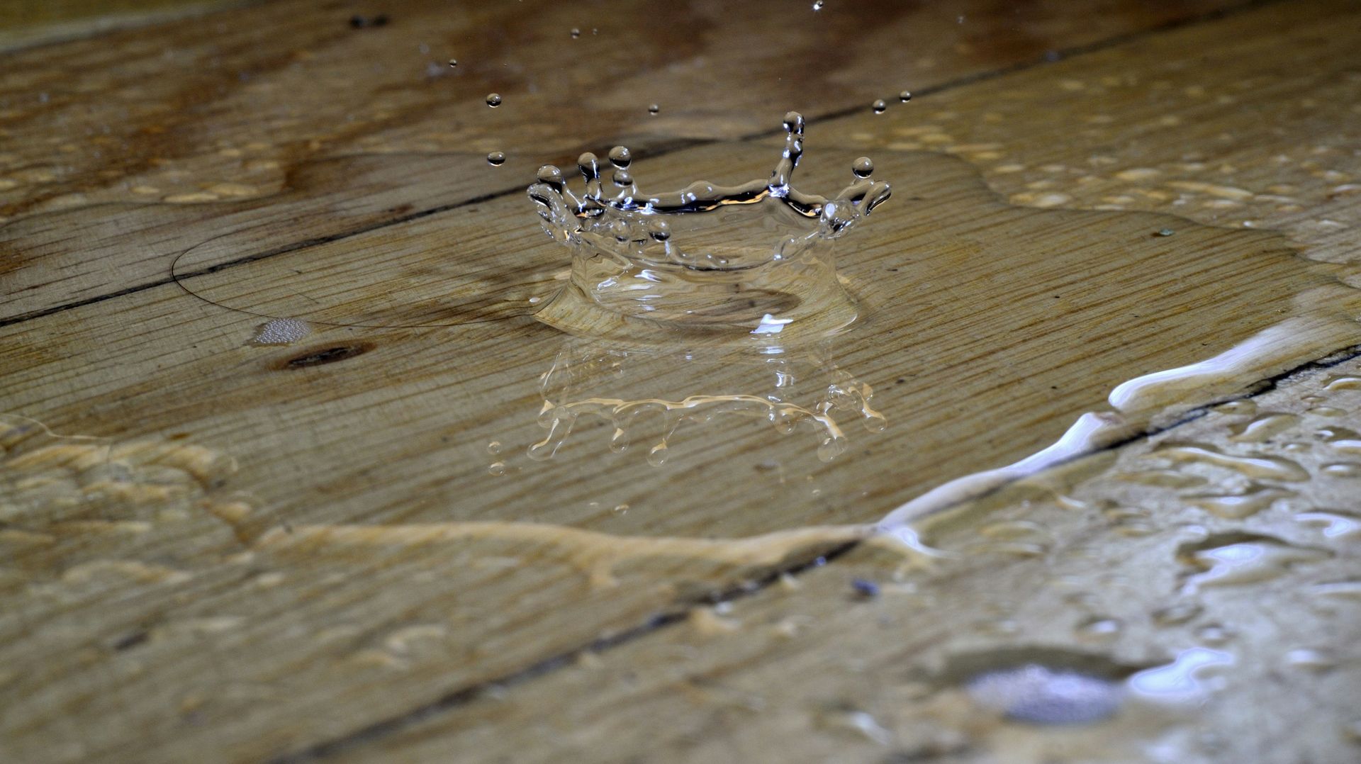 Water droplet splashing on a wet, wooden surface, creating a crown-like shape.