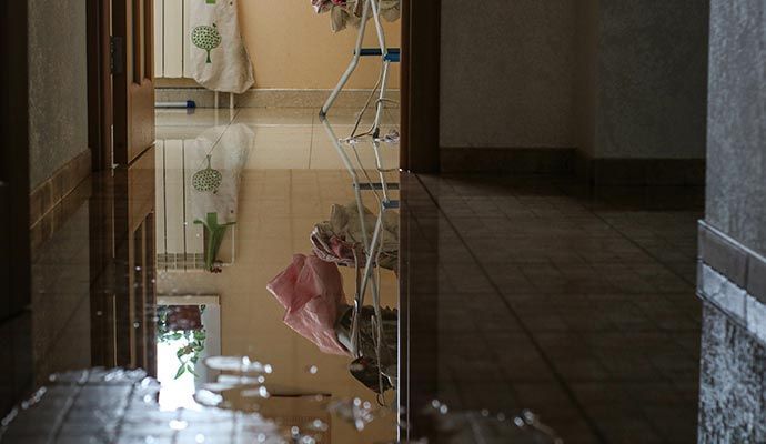 Reflection of a room flooded with water, showing towels, a drying rack, and tile floor.