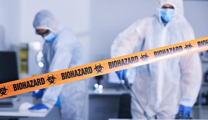 Two people in hazmat suits disinfecting a room behind a biohazard tape barrier.