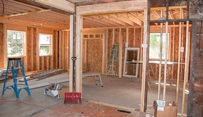 Interior of a house under construction. Wooden studs, ladder, and tools scattered throughout the unfinished space.