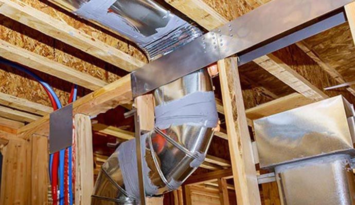 HVAC ductwork installation in a wood-framed ceiling with metal straps and duct tape for support.