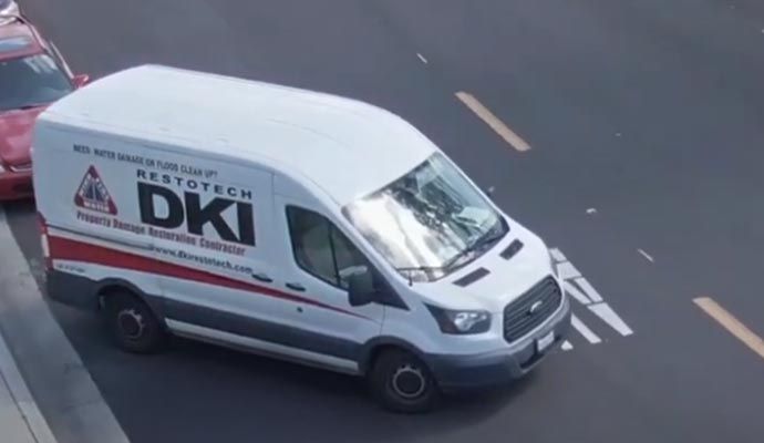 White van with DKI Restotech logo parked next to a curb and a red car.