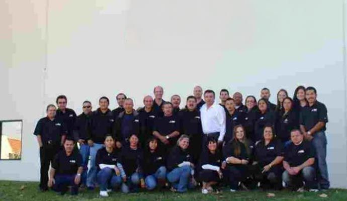 Group of people in black shirts posing in front of a white wall, some kneeling.