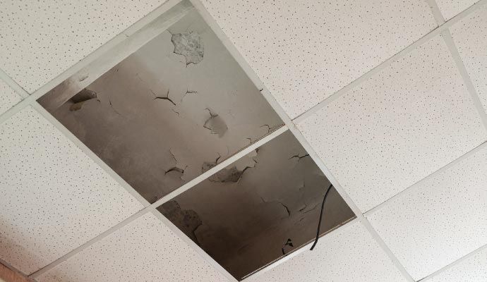 Damaged drop ceiling with a large square missing, showing a dark void above.