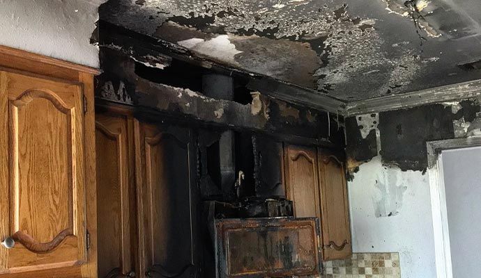 Kitchen cabinets and ceiling damaged by fire; soot and char visible.