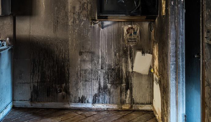 Burned interior of a room, walls charred and stained with smoke, a partially intact sign and a hanging paper.