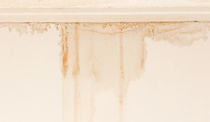 Water damage on a wall with brown stains dripping down from the ceiling and trim.