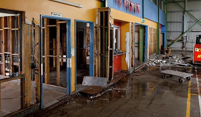 Interior of a damaged building, walls ripped open, flooded floor, debris scattered.