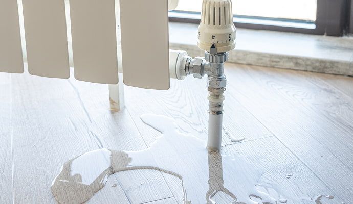 Water leaking from a radiator onto a light wood floor.