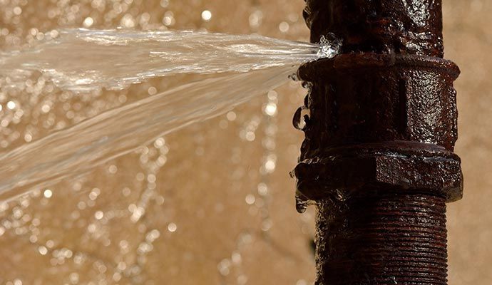 Water spurts from a rusty pipe joint, spraying water outward.