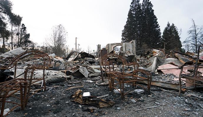 Burned remains of a house after a fire, with charred furniture and debris scattered on the ground.