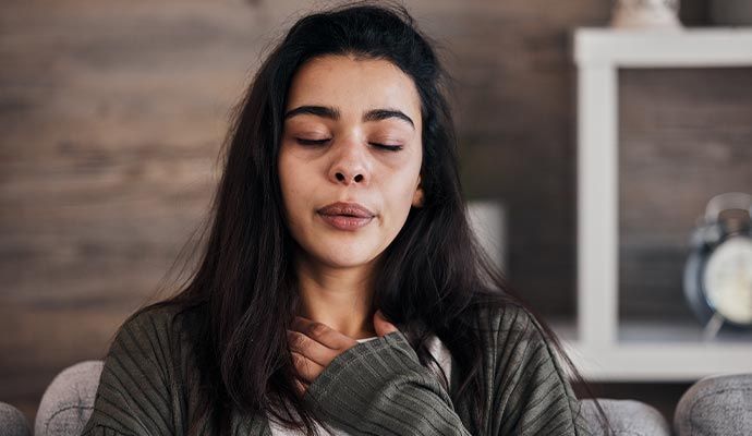 Woman with eyes closed, hand on neck, appearing to be unwell.