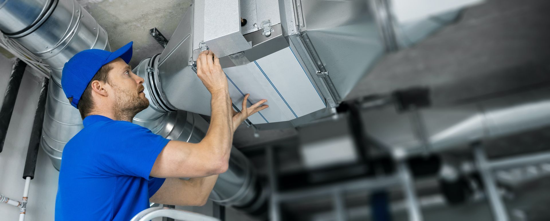 A man is working on a ventilation system in a building HVAC.