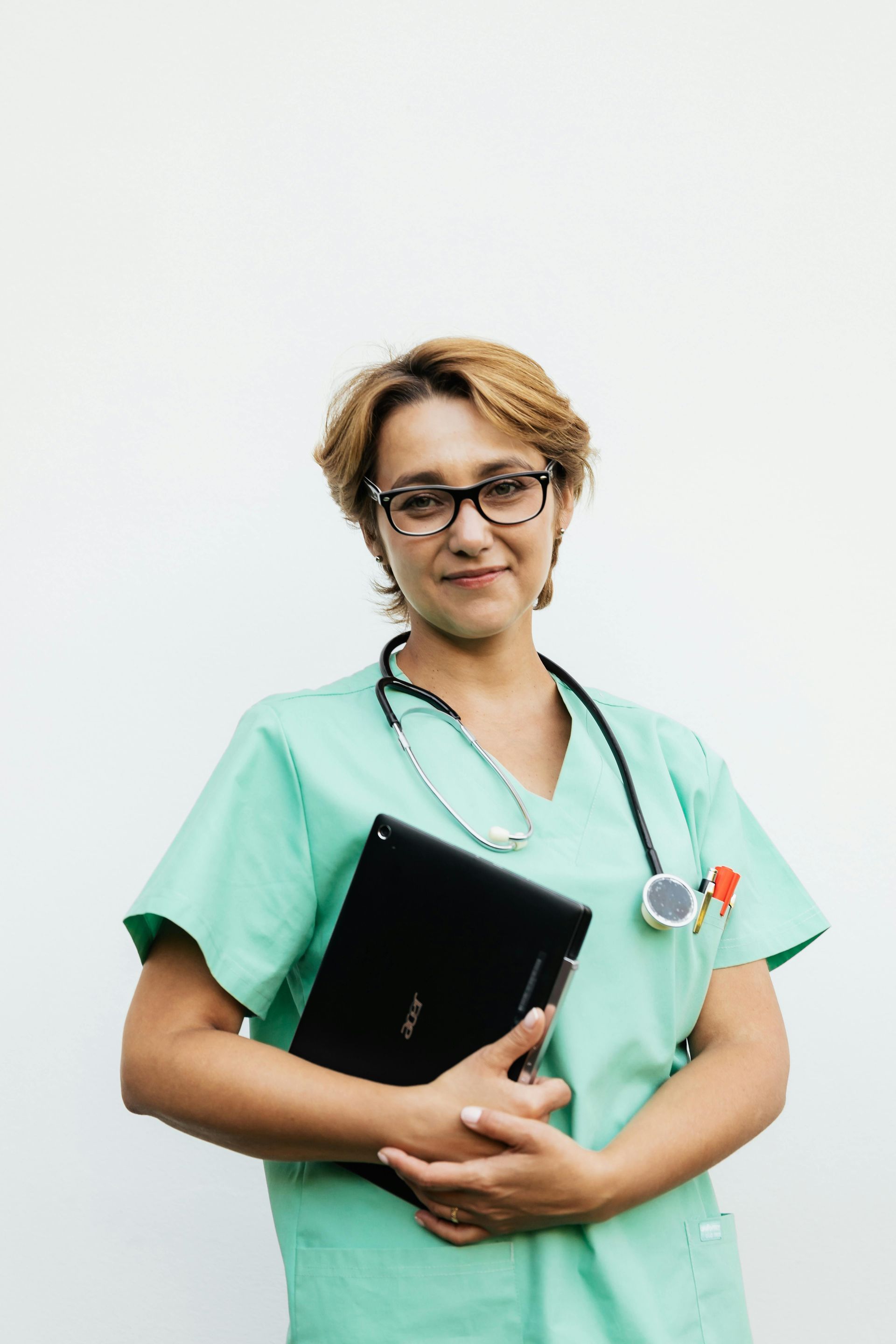 A Nurse  in a green scrub is holding a laptop and a stethoscope.