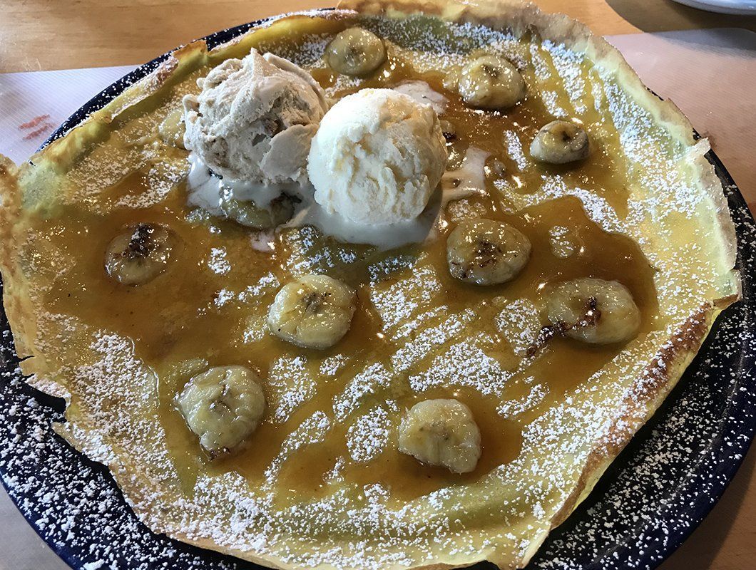 A pancake with bananas and ice cream on top on a plate.