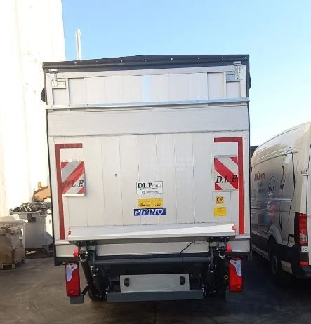 Un furgone bianco con un sollevatore sul retro è parcheggiato in un parcheggio