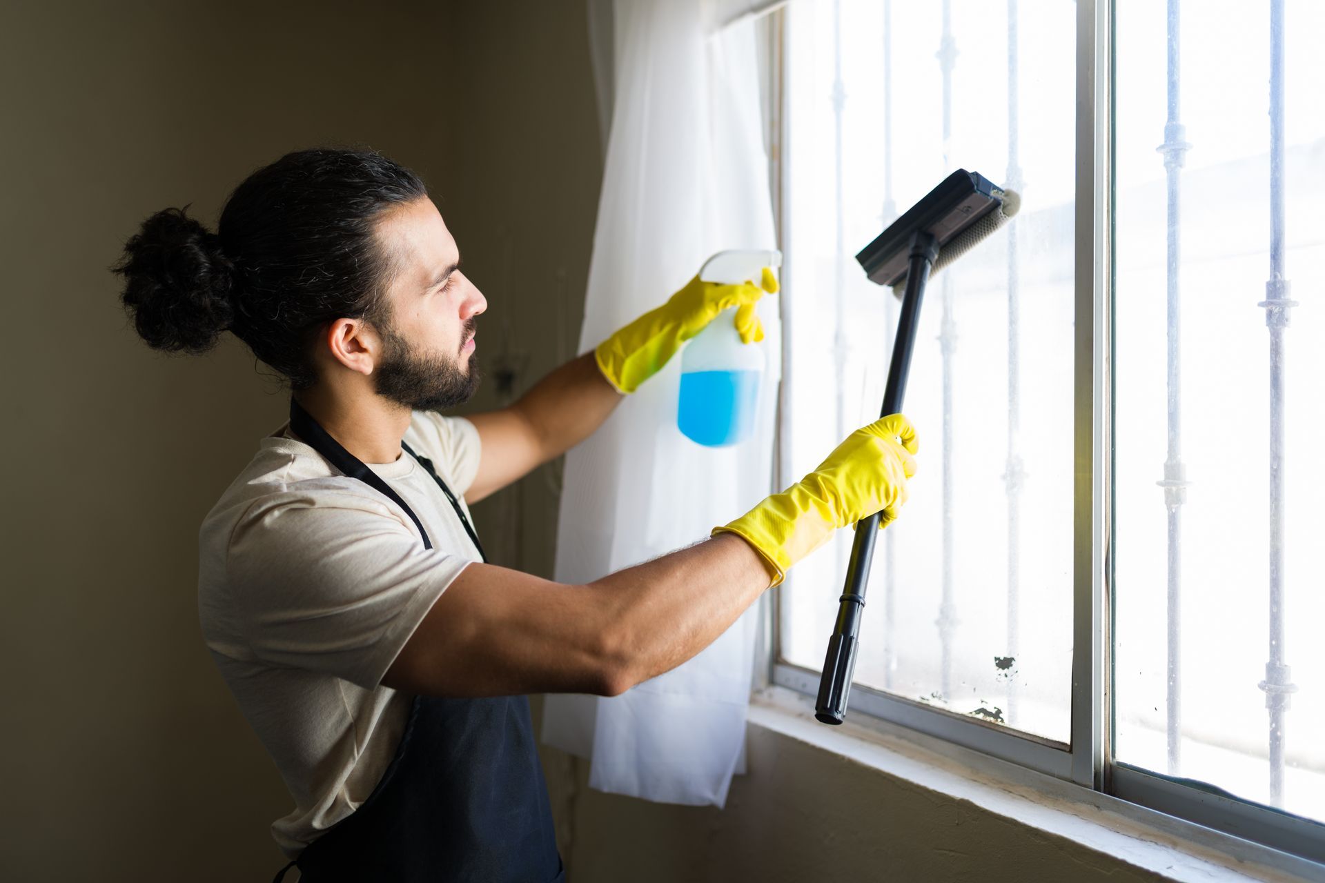 Young male window cleaner at a residential site, wearing apron and yellow gloves.