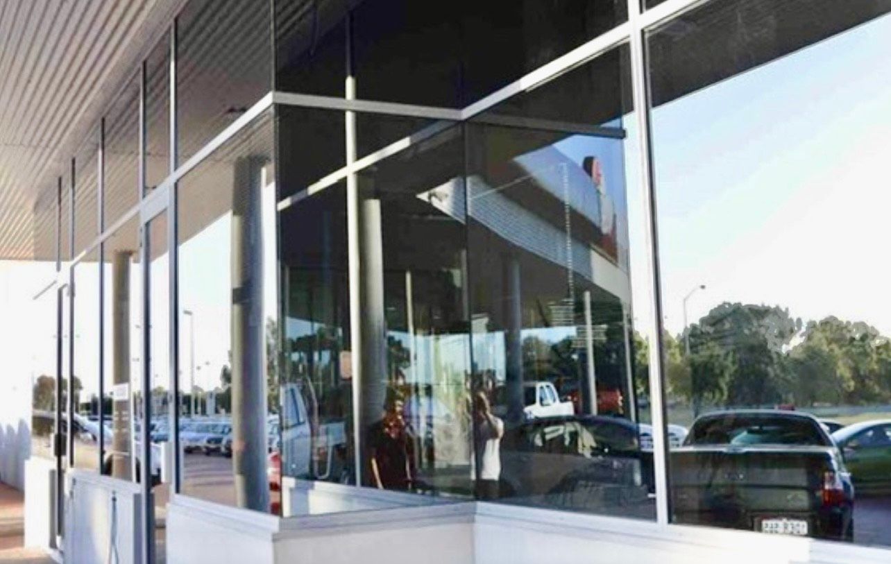 Glass storefront reflects cars and building; exterior view.