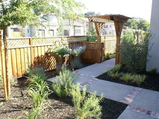 Backyard with a wooden fence, vibrant plants, and a pergola, by Turfworks Inc, a landscape company in Vacaville, CA.