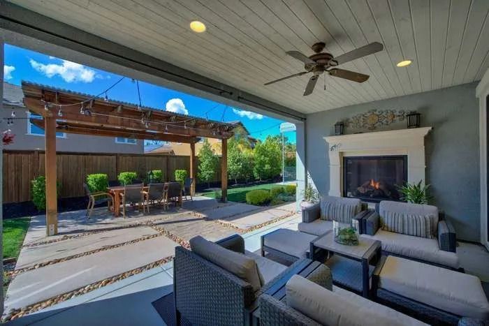 Outdoor living space featuring a covered patio, a fireplace, a dining area under a pergola, set within a landscaped garden
